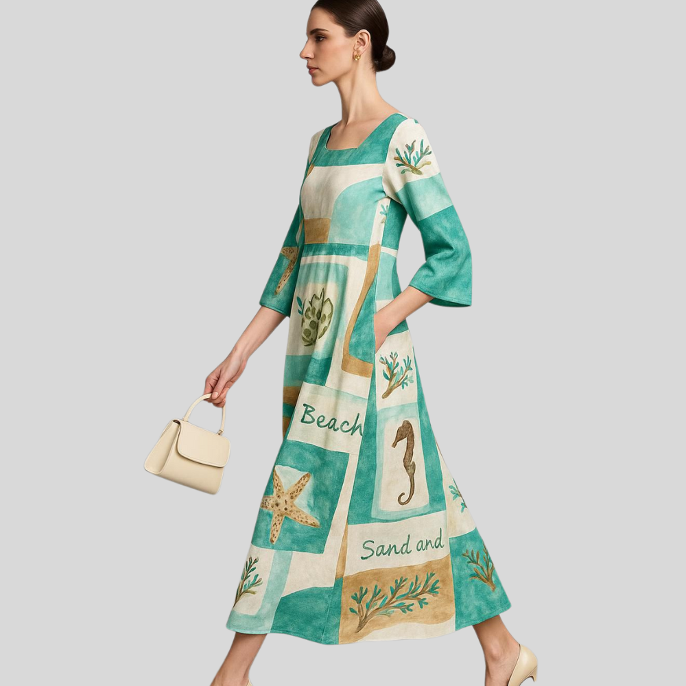 “Model wearing a teal and sand patchwork linen dress with beach-themed motifs, walking with a cream handbag against a light grey background